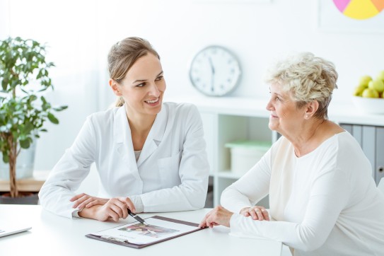 Ärztin erklärt etwas einer älteren Patientin anhand von Unterlagen