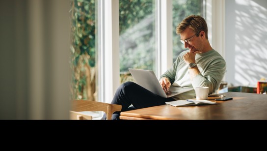 Mann sitzt am Esstisch und scrollt am Computer